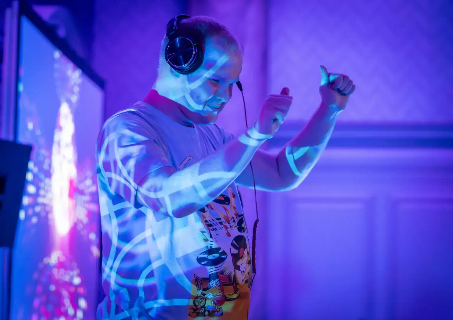 A man wearing headphones closes his eyes and dances. Blue light shines on him.