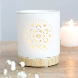 A white wax melt burner with a mandala carved into it. The burner has a wooden base.