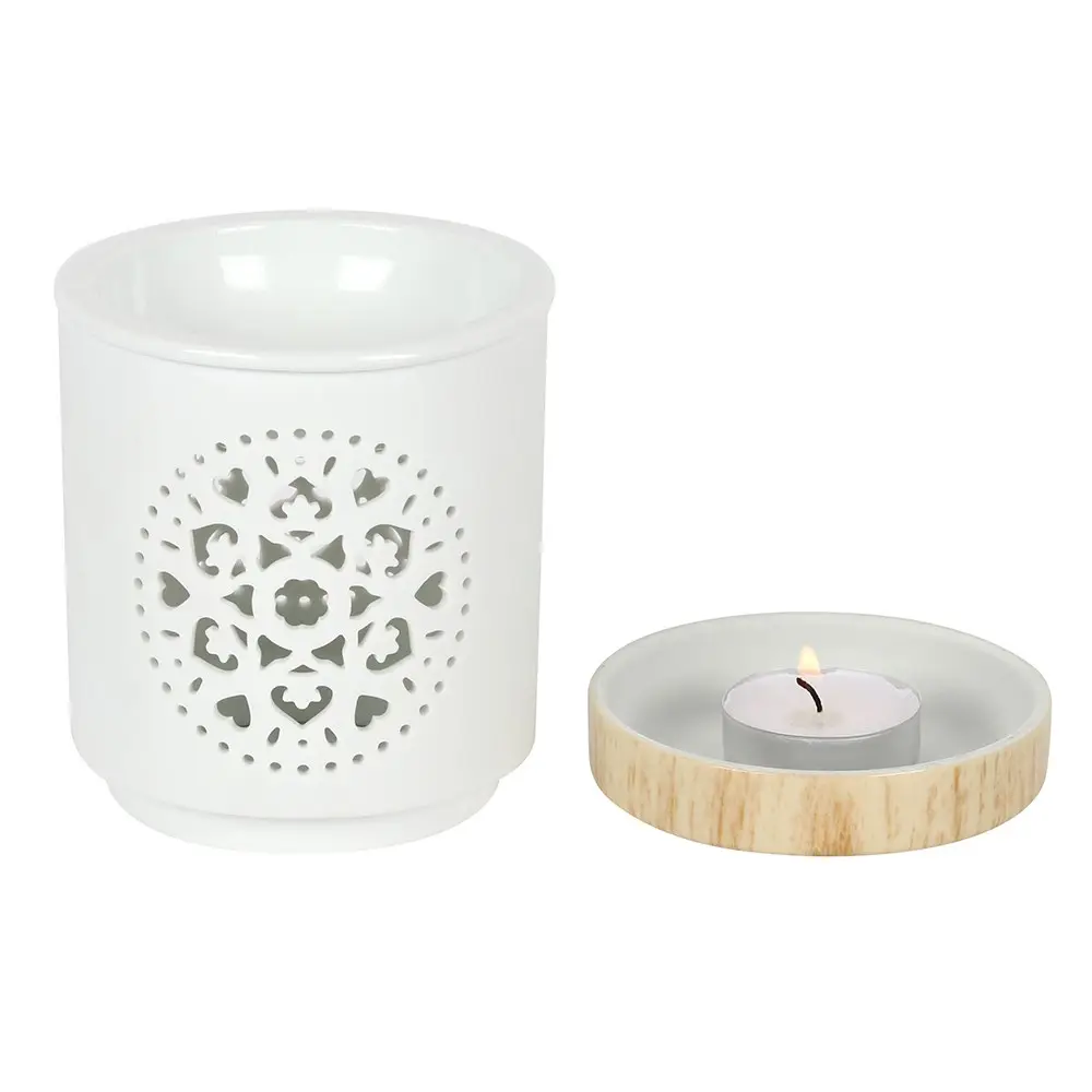 A white wax melt burner with a mandala carved into it. The burner has a wooden base. In this photo, the base has been detached to show the inside of the burner.